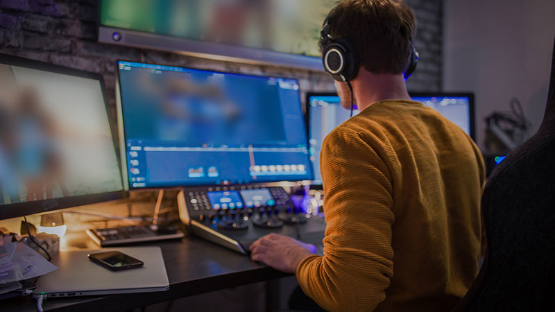 A video producer sits at a workstation compiling source material for his next production