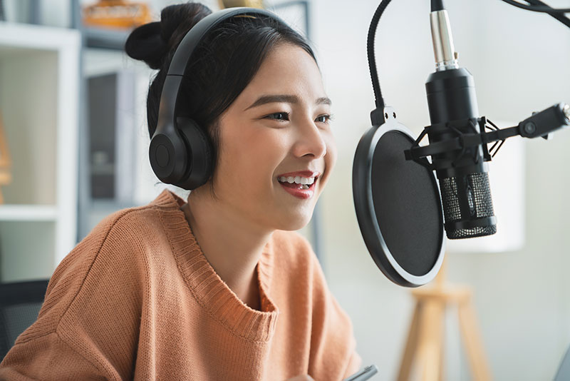 A smiling woman wearing headphones speaks into a studio microphone