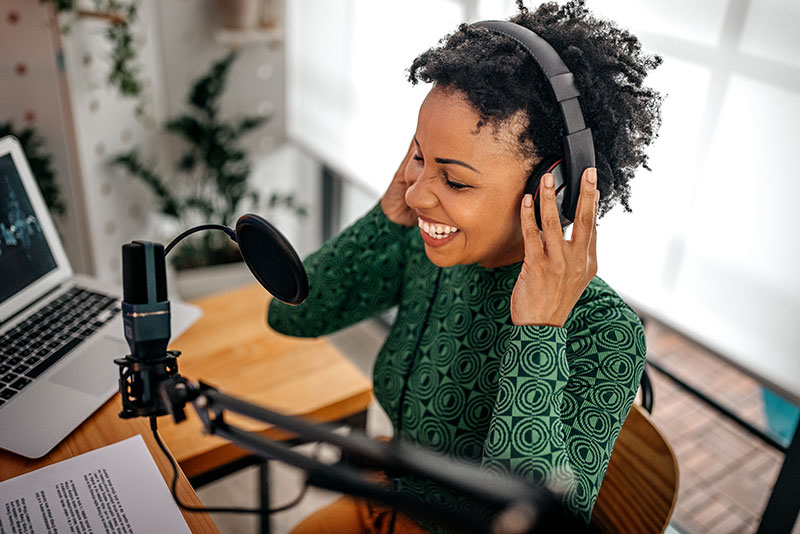 Smiling woman sits in front of a mic while listening with headphones